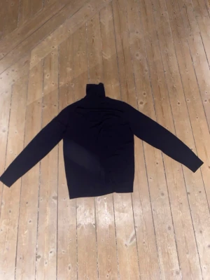 Svart polotröja av cashmere från arket - Snygg svart polotröja av cashmere med lång ärm och klassisk hög krage. Perfekt för lager-på-lager och passar till både jeans och kostymbyxor. Materialet känns mjukt och stretchigt, vilket gör den skön att bära under kyliga dagar.