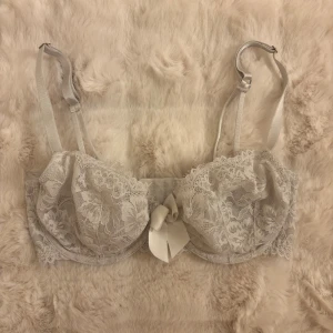 Vit spets-bh med rosett - Söt vit bh i spets med blommigt mönster och en stor rosett framtill. Justerbara axelband och hakknäppning bak. Spetsen ger en romantisk vibe och bh:n har fina detaljer som gör den extra speciell.