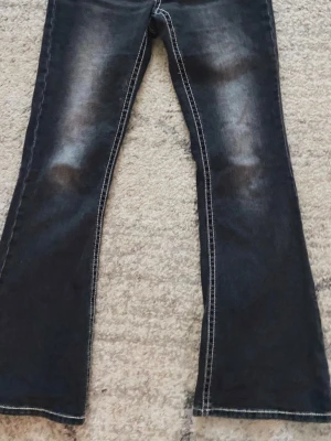 Bootcut svarta jeans med kontrastsömmar från Gina Tricot  - Svarta bootcut jeans med tydliga kontrastsömmar och lätt slitning på framsidan. Jeansen har en klassisk femficksdesign och är tillverkade i ett robust denimtyg som ger en cool vibe. Perfekt för dig som gillar retrostil och vill sticka ut lite extra. Säljer pga att de är för korta.