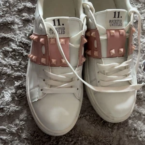 Valentino Rockstud sneakers vit/rosa - Snygga Valentino Rockstud Untitled sneakers i vitt skinn med ljusrosa band och nitar över vristen. Storlek 37-38 Lite smutsiga skosnören men det går att tvätta