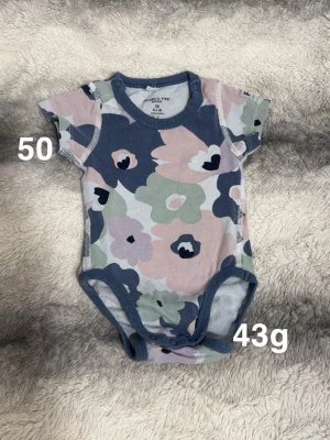 Blommig body från Polarn O. Pyret - Säljer en söt body från Polarn O. Pyret i storlek 50 med blommigt mönster i blå, rosa, grön och vit. Bodyn har korta ärmar och praktiska tryckknappar i grenen. Perfekt för små bebisar och supermjuk mot huden.🌸 Fint använt skick. Har blivit något mörkare. Storlek 50.