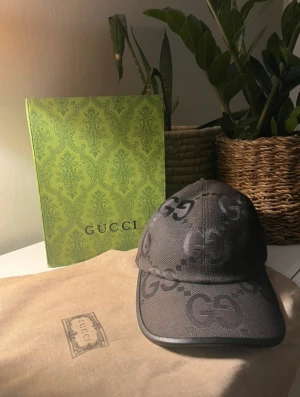 Svart keps med GG-mönster från Gucci - KAN DISKUTERA PRISET PRIVAT                                                                        Snygg svart keps från Gucci med klassiskt GG-mönster i mörkgrått. Justerbar rem bak i svart läder med metallspänne. Tillverkad i Italien och levereras med original dustbag och box. Perfekt för dig som vill ha en lyxig streetstyle-accessoar.
