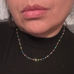 Färgglad kedjehalsband  - Säljer ett tunt halsband med små pärlor i olika färger som blå, rosa, gul, vit och orange. Kedjan är i guldton och har en enkel karbinlås. Perfekt för dig som gillar färg och vill ha något som sticker ut.