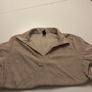 Beige frotté pikétröja från SOC - Säljer en beige pikétröja från SOC i storlek S. Tröjan är gjord i mjuk frotté och har klassisk krage med v-ringad öppning. Perfekt för dig som gillar chill och sportig stil. Enkel att matcha med jeans eller shorts.