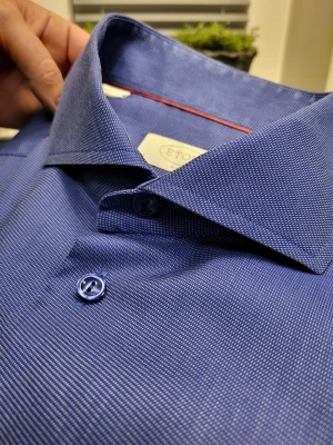 Blå slim fit skjorta från Eton 42 16.5 - Snygg blå skjorta från Eton i slim fit med diskret mönster och klassisk krage. Skjortan har långa ärmar, blå knappar och är tillverkad i bomull. Perfekt för dig som gillar stilrena och moderna plagg.