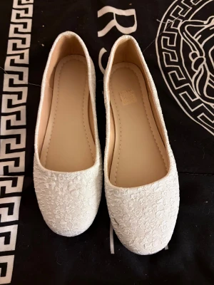 Vita blommiga ballerinaskor strl 40 - Säljer ett par vita ballerinaskor med blommigt broderat mönster. Skorna har rund tå och platt sula,  Perfekt för dig som gillar en romantisk och clean stil. Snygga till både jeans och klänning. Finns en nackdel (se sista bilden). De har ett svart streck på ena skon.   Vet dock inte hur man får bort den.