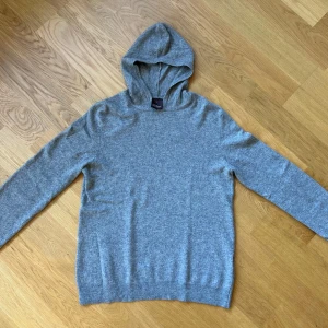 Grå kashmir hoodie från Oscar Jacobson - Säljer en stilren grå hoodie från Oscar Jacobson. Tröjan är tillverkad i Italien och har en klassisk design med långa ärmar och en bekväm huva. Perfekt för en avslappnad look. I Kashmir orginal pris 1700 KR