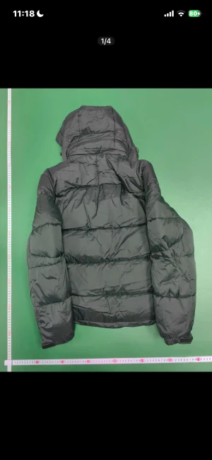 Svart dunjacka från Polo Ralph Lauren - Svart dunjacka från Polo Ralph Lauren med huva och röd logga på bröstet. Jackan har quiltad design, dragkedja framtill och två sidofickor med dragkedja. Perfekt för kalla dagar och har en clean, sportig look som funkar till streetwear.