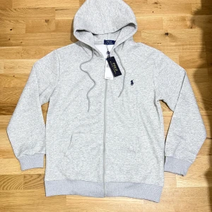 Ralph Lauren Grå Zip Hoodie - Grey Ralph Lauren Polo Zip Hoodie Klassisk och bekväm zip-hoodie från Ralph Lauren i stilren grå färg. Mjuk, varm och perfekt för både vardag och chill. En mångsidig och snygg hoodie som passar extra bra under vintern och inför julens alla tillfällen.  TVEKA INTE ATT SKICKA EN BUD:)