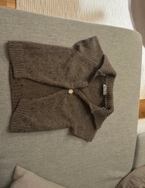 Brun stickad kofta - Kortärmad brun stickad kofta från Zara med en stor dekorativ knapp framtill. Koftan har en bred krage och ribbade kanter vid ärmslut och nederkant. Perfekt för lager-på-lager och en chill höstlook.