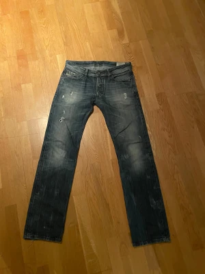 Diesel Larkee jeans - Säljer ett par skit snygga Diesel Larkee jeans i jättesnygg wash med slitna detaljer och raka ben. Jeansen har klassisk femficksdesign, silverfärgade knappar på bakfickorna och en cool Diesel-label bak i midjan. Sitter som en blandning av straight och slim.