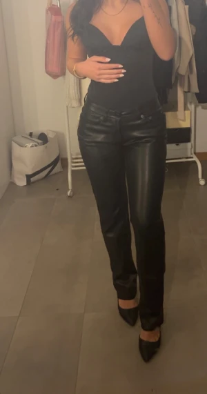 Svarta raka skinnbyxor - Säljer ett par svarta skinnbyxor med rak passform och klassisk midja. Byxorna har snygga detaljer med fickor fram och bak samt knapp och dragkedja. Perfekta för dig som vill ha en edgy och stilren look.