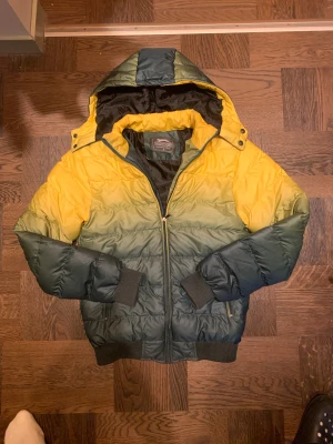 Gul och grön pufferjacka från Slazenger - Säljer en fet pufferjacka från Slazenger i storlek S. Knappt använt. Jackan har cool färgskiftning från gul upptill till mörkgrön nedtill, med huva och dragkedja framtill. Huvan går att ta bort kolla bild 4. Ribbstickade muddar vid ärmar och nederkant, samt praktiska fickor med dragkedja. Perfekt för kalla dagar. Vid frågor, hör av dig! 