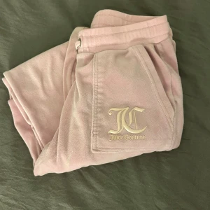 Rosa mjukisbyxor Juicy Couture - Supermysiga rosa mjukisbyxor från Juicy Couture med broderad JC-logga på benet och snörning i midjan. Byxorna har en klassisk relaxed fit och är tillverkade i mjuk fleece för maximal komfort. Perfekta för chill dagar eller när du vill ha en avslappnad look.