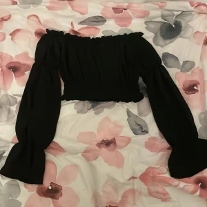 Svart offshoulder croppad topp - Säljer en svart offshoulder topp med långa puffiga ärmar och croppad passform. Toppen har volangdetaljer.