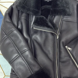 Svart teddyjacka från ONLY - Säljer en svart teddyjacka från ONLY med mjuk fuskpäls på kragen och insidan. Jackan har coola silverfärgade dragkedjor, markerade sömmar och en oversized look. Perfekt för dig som vill ha en trendig och varm jacka med streetkänsla.