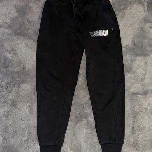 Svarta mjukisbyxor från Hoodrich S - Svarta mjukisbyxor från Hoodrich i storlek S. Byxorna har resår och snörning i midjan, muddar vid bensluten och Hoodrich-logga i vitt och silver på ena benet. Tillverkade i bomull och polyester för en skön och avslappnad känsla.