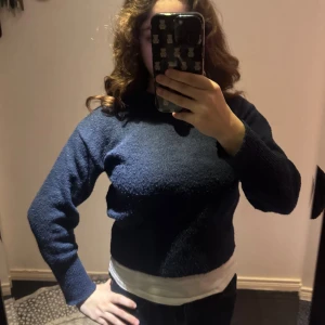 Mörkblå stickad hoodie från Gina Tricot - Mysig mörkblå stickad hoodie från Gina Tricot med huva och långa ärmar. Tröjan har en enkel och stilren design med ribbade muddar och en skön, loose passform. Perfekt för kyliga dagar när du vill vara både bekväm och snygg.