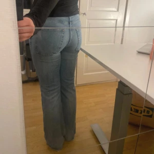 Ljusblå bootcut jeans - Säljer ett par ljusblå jeans med bootcut passform och klassisk femficksdesign. Jeansen har normal midja och är tillverkade i mjukt denimtyg som ger en avslappnad vibe. Perfekta för dig som gillar en retroinspirerad look med lite utsvängda ben. Jag är ca 162 cm lång