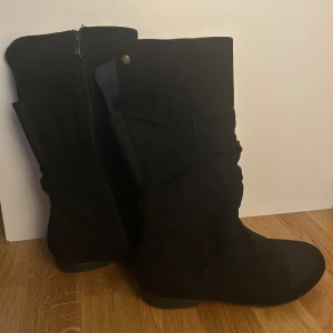 Svarta mockastövlar med dragkedja - Snygga svarta stövlar i mocka med platt sula och rund tå. Stövlarna har dragkedja på sidan för enkel på- och avtagning och en stilren, klassisk look som passar till många outfits. Funkar både dam och barn då storlek är 37.