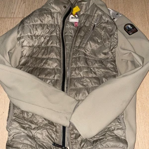 Beige parajumper jacka - Snygg beige pufferjacka från Parajumpers med quiltad front och ärmar i stretchigt material. Jackan har dragkedja, bröstficka med dragkedja och klassisk PJS-patch på ärmen. Perfekt för kyliga dagar och riktigt clean look.