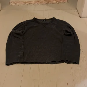 Mörkgrå croppad tröja från Divided - Säljer en mörkgrå croppad tröja från Divided med lång ärm och rund hals. Tröjan har en loose passform och är tillverkad i mjuk bomull. Perfekt för chill dagar och enkel att matcha med jeans eller leggings.