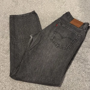 Levi's 551 grå jeans straight fit - Snygga grå jeans från Levi's modell 551 med klassisk femficksdesign och rak passform. Jeansen har en mörkgrå tvätt och är tillverkade i slitstarkt denim. Perfekta för en avslappnad och cool look.
