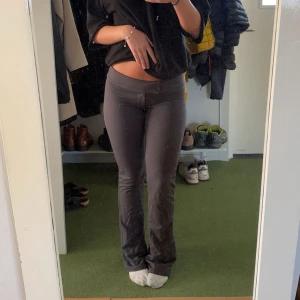 Mörkgrå byxor  - Säljer ett par mörkgrå mjukisbyxor med bootcut-modell och låg midja. Byxorna har en tight passform upptill som släpper ut vid bensluten. Perfekta för en chill och avslappnad stil.