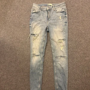 Ljusblå slitna skinny jeans - Säljer ett par ljusblå skinny jeans med slitningar och trasiga detaljer på benen. Jeansen har klassisk femficksdesign, normal midja och dragkedjegylf. Perfekta för en avslappnad och trendig look.