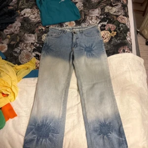 Blå och vita jeans med blommönster - Unika jeans i ljusblå och vit tvätt med coola blommönster på låren och benen. Modellen har raka ben och klassisk femficksdesign. Perfekta för dig som vill sticka ut med en kreativ och trendig look.