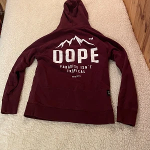 Vinröd hoodie från Dope med tryck - Säljer en vinröd hoodie från Dope med vit logga och bergstryck på både bröstet och ryggen. Tröjan har huva med snörning och en stor magficka. Perfekt för dig som gillar streetwear och vill ha en snygg och bekväm look.