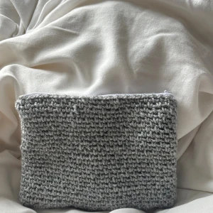 Grå virkad necessär med dragkedja - En handgjord grå virkad necessär med vit dragkedja och ett innerfoder i mörkblått tyg med små prickar. Perfekt för att förvara småsaker eller smink. Den mjuka virkade ytan ger en mysig och unik känsla.