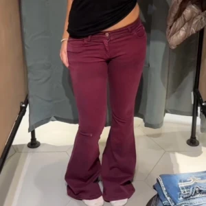 Vinröda bootcut jeans från Miss Sixty - Säljer ett par vinröda jeans från Miss Sixty i klassisk bootcut-modell. Byxorna har låg midja, fem fickor och snygga detaljer med röda logotaggar. Materialet är mjukt och stretchigt bomullstyg, tillverkade i Italien. Perfekt för dig som gillar retrovibe och färg!