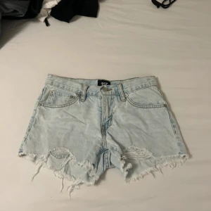 Ljusa jeans shorts från 157 med slitningar - Säljer ett par ljusblå jeans shorts från 157 med hög midja. Shortsen har råa, fransiga kanter och slitna detaljer framtill för en avslappnad vibe. Klassisk femficksmodell med dragkedja och knapp. Perfekta för sommardagar! Pris kan diskuteras 🥰