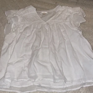 Vit blus med volang från Gina Tricot - Säljer en söt vit blus från Gina Tricot i storlek 158/164. Blusen har korta volangärmar, v-ringad hals och fina broderade detaljer upptill. Luftigt material som känns skönt mot huden och ger en flowy känsla. Perfekt för dig som gillar en romantisk och fräsch stil.