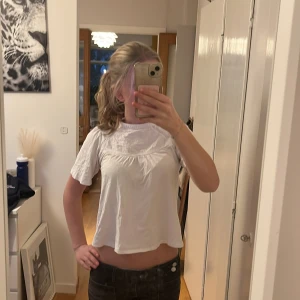 Zara blus - Säljer en söt vit blus med korta ärmar och rund hals. Blusen har fina spetsdetaljer och broderade mönster framtill som ger en romantisk vibe. Den är croppad och har knapp i nacken för enkel påklädning. Perfekt till jeans eller kjol!