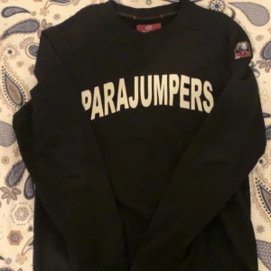 Svart sweatshirt från Parajumpers - Svart sweatshirt från Parajumpers med stor vit logotyp på bröstet och patch på ärmen. Tröjan har rund hals och långa ärmar, perfekt för dig som gillar stilrena och sportiga plagg. Skön passform och klassisk look.