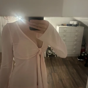 Ljusrosa omlottklänning Gina Tricot - Supersöt ljusrosa omlottklänning från Gina Tricot i storlek XS. Klänningen har långa ärmar, v-ringning och knyt framtill som ger en snygg och feminin look. Säljer för att den inte kommer till användning!🫶