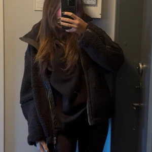 Brun teddyjacka med dragkedja - Mysig brun teddyjacka med oversized passform och lång ärm. Jackan har en rejäl dragkedja framtill och är tillverkad i fluffigt teddy-material som håller dig varm under kyliga dagar. Perfekt för dig som gillar en avslappnad och trendig stil.