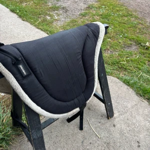  Barbacka pad k fint Skick - Bilderna visar en sadelpad från onehorse , med svart ovansida och mjuk, vit undersida i syntetpäls. Produkten ser ut att vara i gott skick utan synligt slitage eller defekter. Perfekt för extra komfort och skydd för hästen vid ridning.