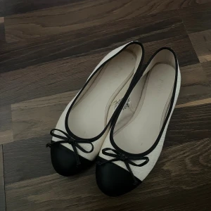 Svartvita ballerinaskor från Primark - Stilrena ballerinaskor från Primark i beige tyg med svarta detaljer och rund tå. Skorna har svart tåparti i syntet, svart kant och en söt rosett framtill. Perfekta för dig som gillar klassisk och enkel stil.
