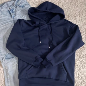 Mörkblå hoodie med huva och ficka - Säljer en mörkblå hoodie med huva och snörning. Tröjan har en stor magficka och ribbade muddar vid ärmslut och nederkant. Perfekt för chill dagar och enkel att matcha med jeans eller joggers.