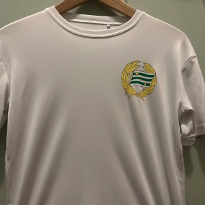Vit Hammarby fotbollströja Craft 158/164 - Vit fotbollströja från Craft med Hammarby IF:s klubbmärke på bröstet. Tröjan är kortärmad och tillverkad i ett lätt, sportigt material som andas. Perfekt för träning eller match. Klassisk rund hals och diskret Craft-logga på ärmen.