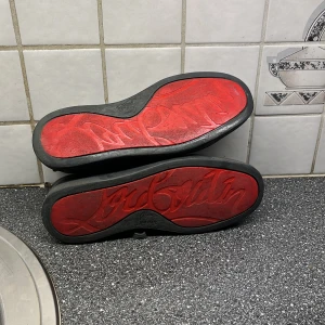 Christian Louboutin grå mockasneakers - Säljer ett par  grå  sneakers från Christian Louboutin i mocka med klassisk röd sula och svarta snören. Skorna har rund tå, platt sula och beige innersida. Kommer med originalkartong och äkthetsintyg. Perfekta för dig som vill sticka ut med exklusiva detaljer. Du får med kvittot o org boxen o allt med 