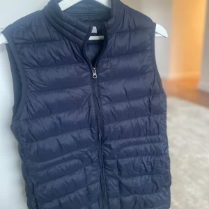 Mörkblå dunväst från Mango Kids - Marinblå väst strl 164 från MNG Kids i quiltad modell. Västen har krage, dragkedja framtill och är lätt vadderad.