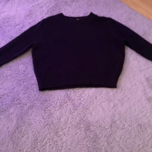 Svart croppad stickad tröja - En svart, croppad stickad tröja med rund hals och långa ärmar. Tröjan har ribbade muddar vid ärmslut och nederkant, vilket ger en snygg och enkel look. Perfekt för lager-på-lager under kyliga dagar.