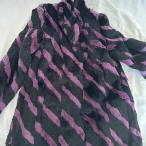 Svart och lila pälsjacka, strl 38 - Säljer en fluffig och unik pälsjacka i svart och lila med zebramönster. Jackan har lång ärm och är riktigt mjuk och skön. Perfekt för dig som vill sticka ut med en cool och färgstark look. Storlek 38. Köpt på hm back in the days 