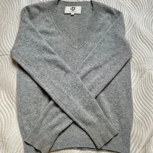 Grå v-ringad tröja 100% cashmere Wakakuu Icons - Snygg grå tröja 100% cashmere från Wakakuu Icons med v-ringad hals och långa ärmar. Tröjan har ribbade muddar vid ärmslut och nederkant