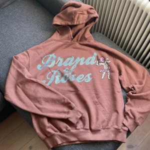 Brun hoodie Brand of Roses S - Säljer en brun hoodie från Brand of Roses i storlek S. Tröjan har stor huva, magficka och tryck med texten 'Brand of Roses' i ljusblått och en tecknad figur på framsidan. Har ej använd den något alls då den var i fel storlek. Köptes för ca 1300 ny. Skriv gärna om du har minsta fundering eller om fler bilder önskas. Prisen kan sänkas vid snabb affär. 😁😁