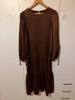 Brun långklänning - Snygg brun långklänning med rund hals och långa ärmar. Klänningen har en volang nedtill 🤎